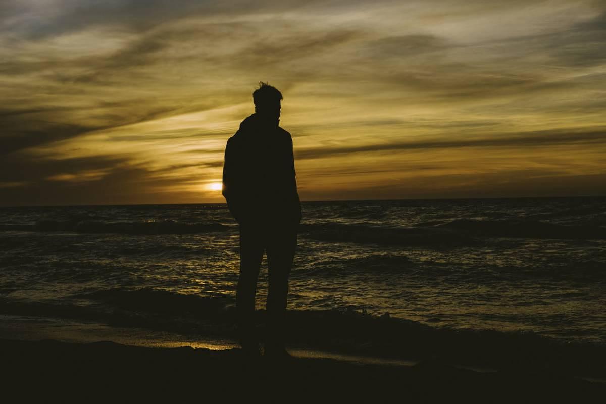 Person standing on seashore during sunset
